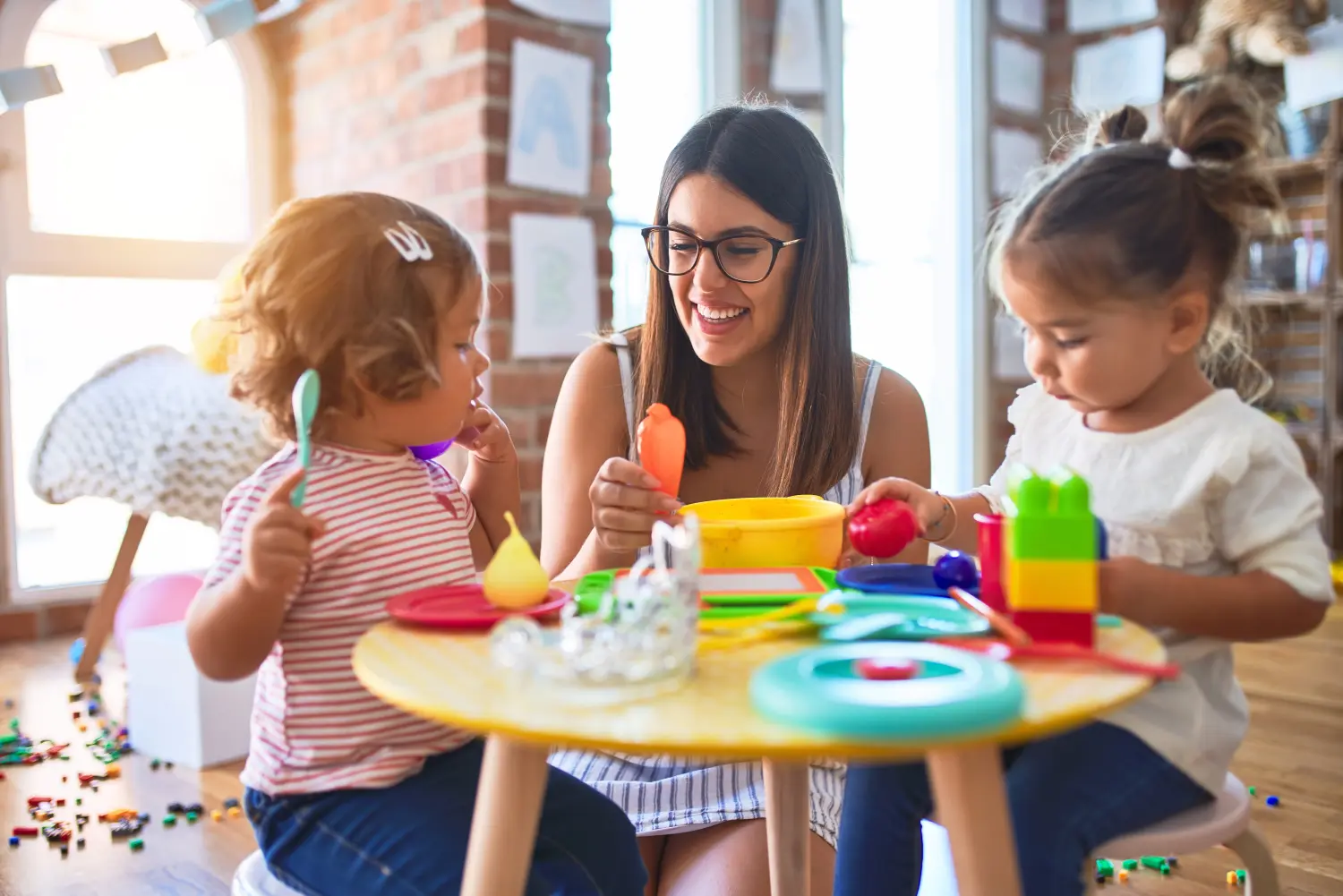 Junge Lehrerin und kleine Kinder spielen mit Spielzeug und Ton